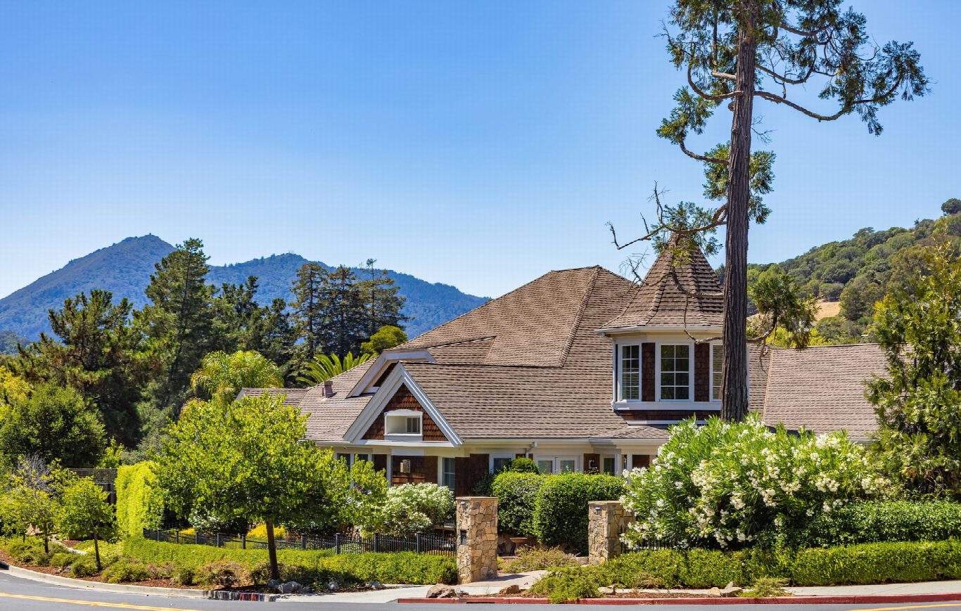 Maison de style cottage entourée de verdure, avec des collines au loin sous un ciel dégagé