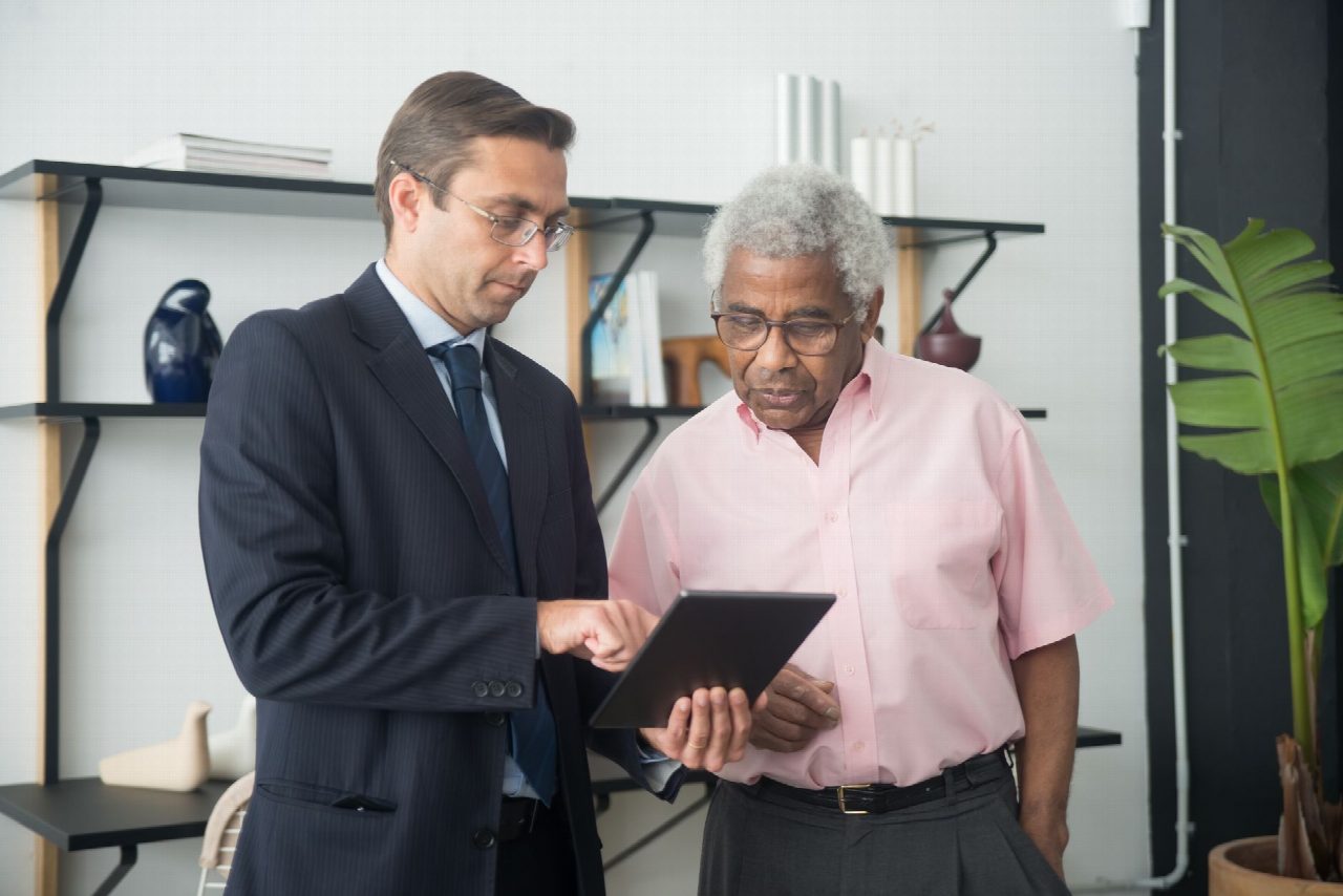 Deux hommes consultent une tablette numérique en discutant de stratégie d’entreprise dans un bureau lumineux.