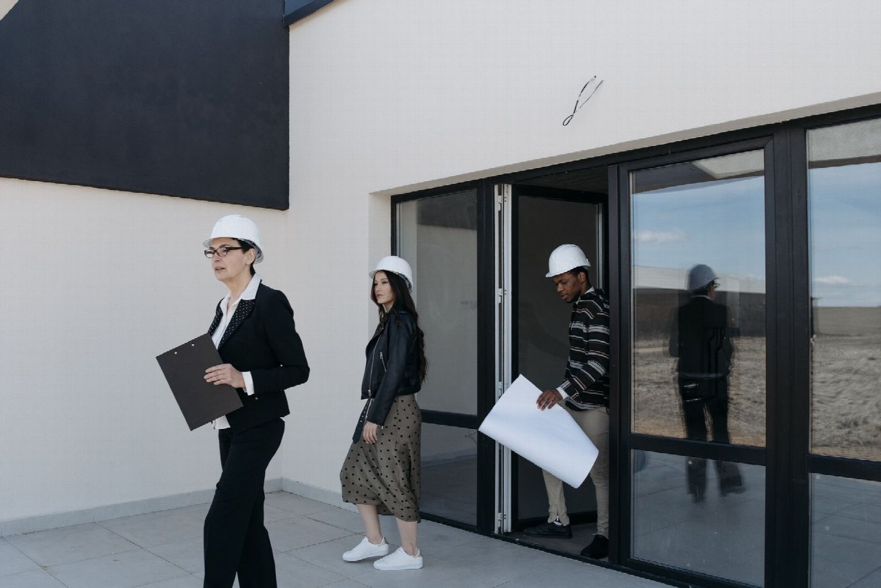 Des professionnels en casque de chantier examinent des plans devant un bâtiment moderne.